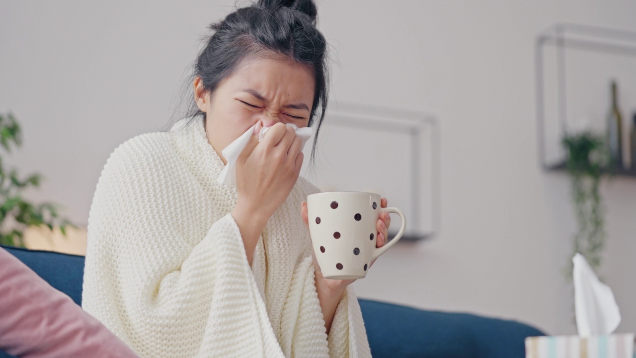 亚洲妇女患普通感冒，打喷嚏在餐巾和喝茶视频素材