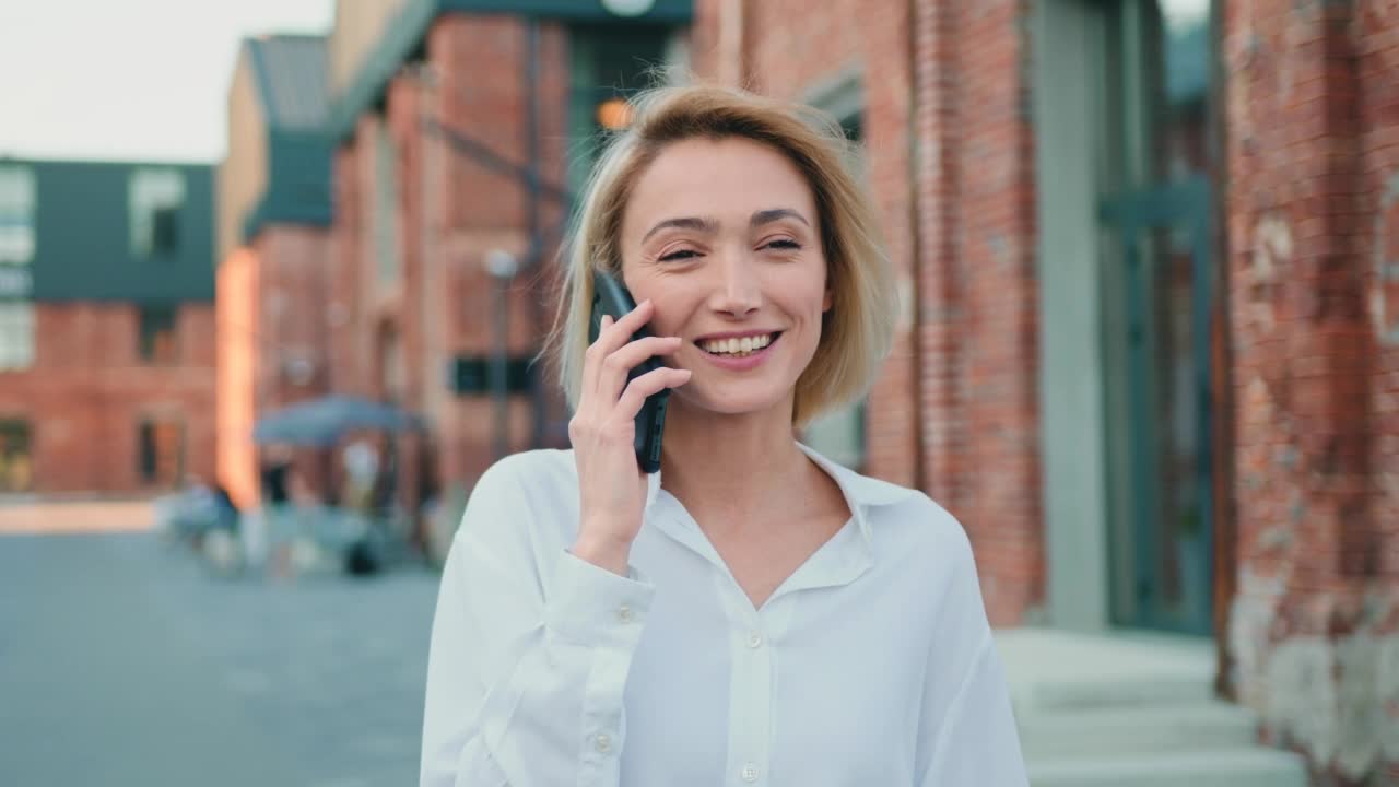 迷人的金发商人的肖像走在街上在城市讲手机。年轻漂亮的女孩在打电话视频素材