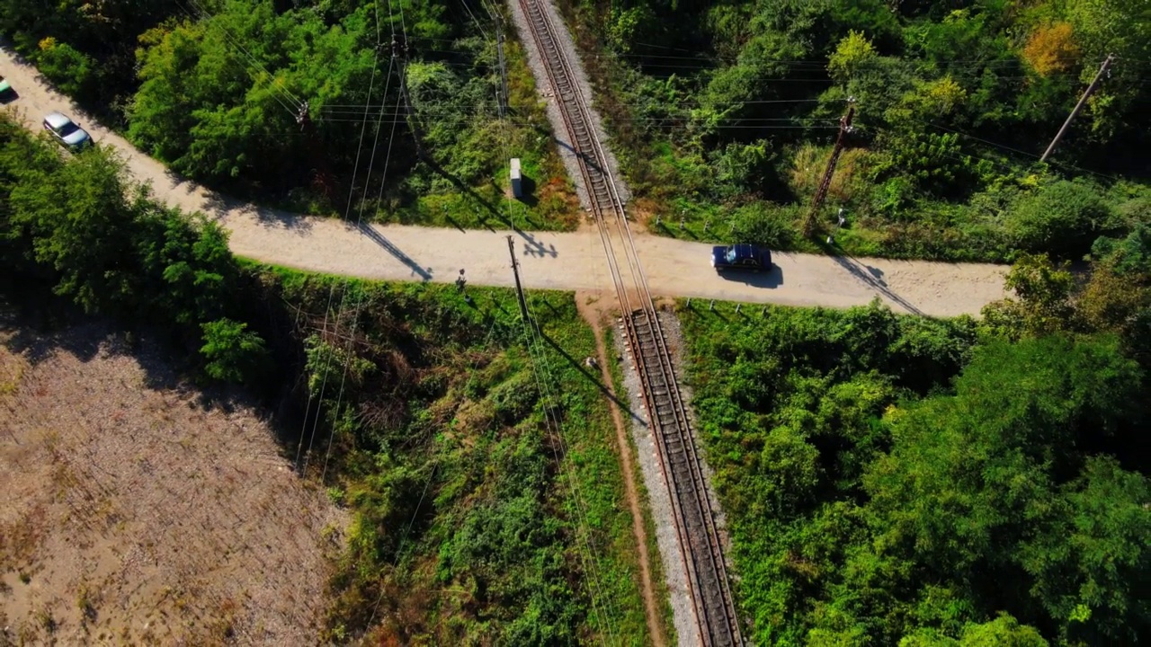 绿色森林中的铁路。汽车行驶在乡间公路上，穿过空荡荡的铁路视频素材