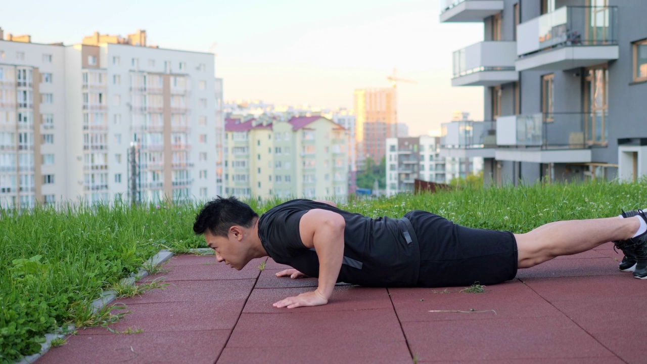 在城市建筑背景下，亚洲人在户外锻炼的侧面视图。男子肖像做俯卧撑在运动场地在睡眠区镇。运动员在户外锻炼。视频素材