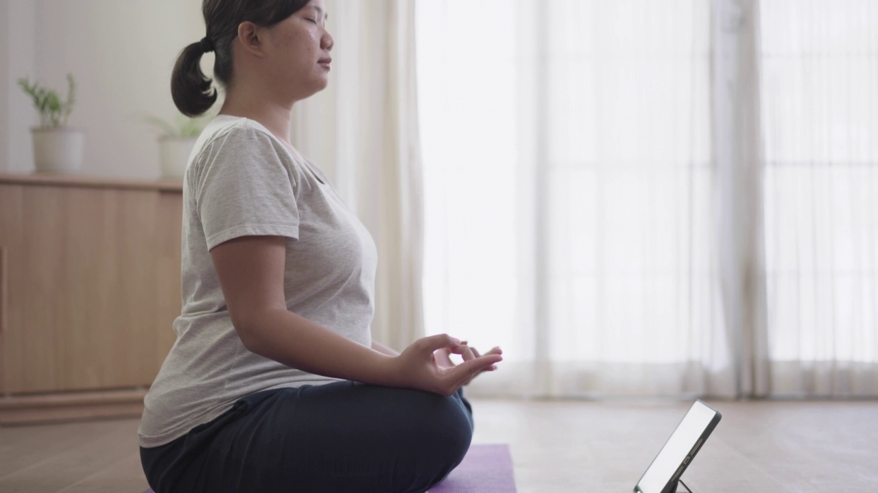 练习瑜伽的女人坐在家里的地板上看在线教程视频素材