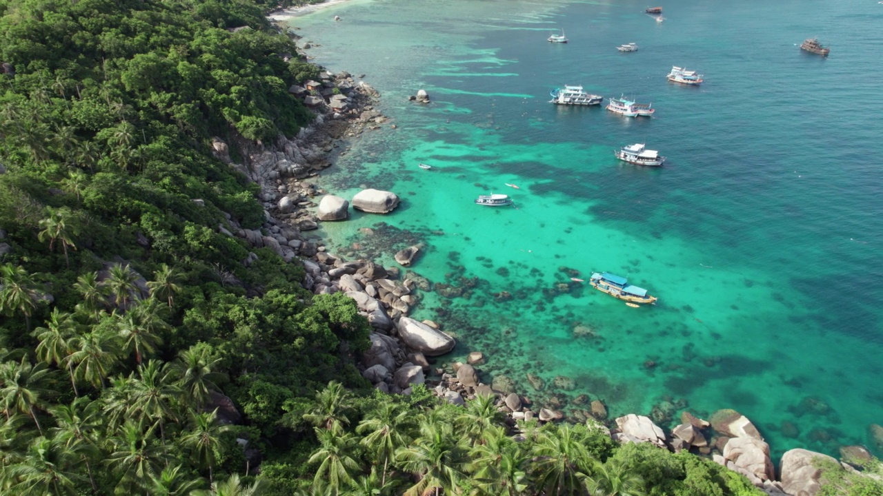 鸟瞰图:夏天的热带海滩天堂，岩石海岸线，椰子树和蓝绿色的海水。船、游艇和帆船在海里，许多珊瑚是潜水员的天堂视频素材