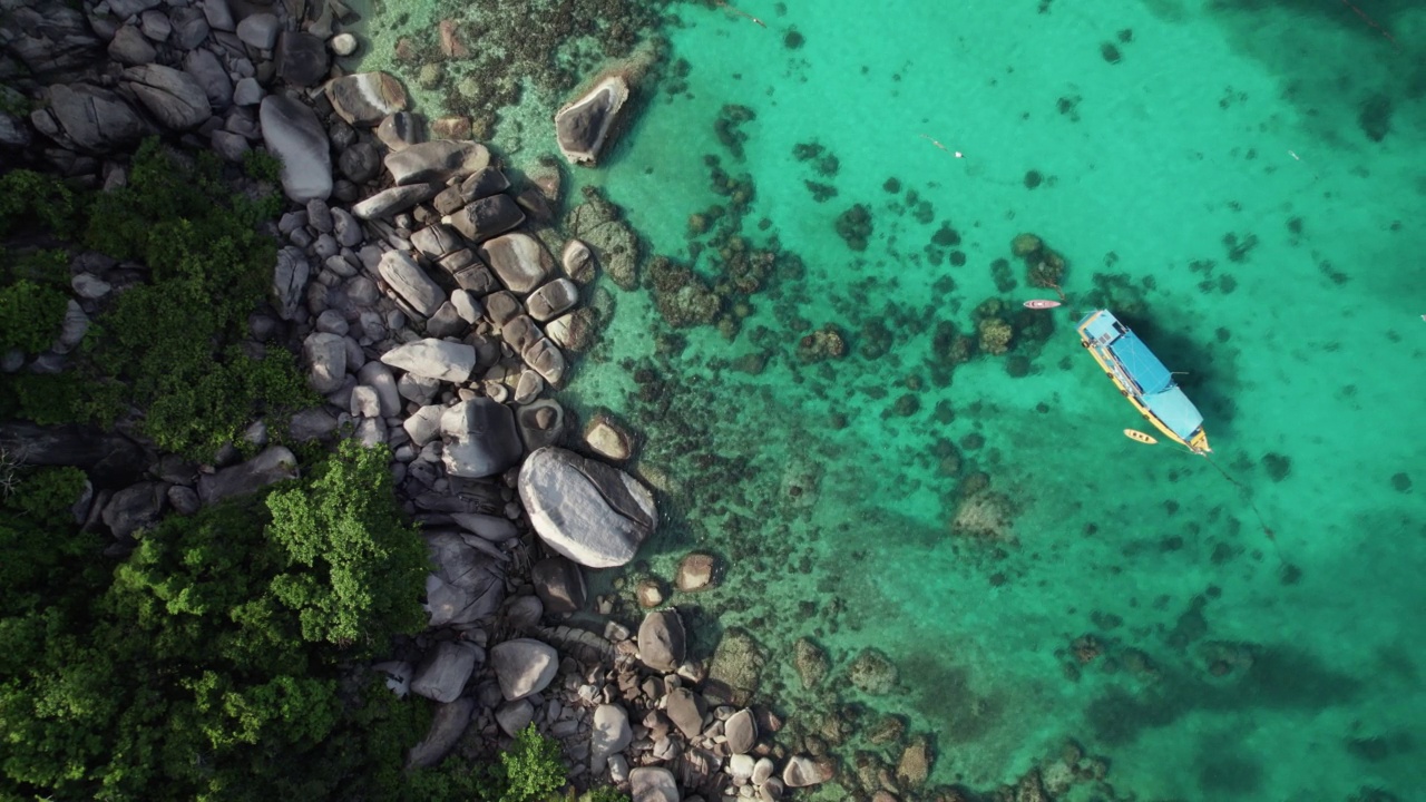 鸟瞰图:热带岩石海滩是夏天潜水者的天堂，还有蓝绿色的海水。海中有一艘船供潜水员探索海底的珊瑚视频素材