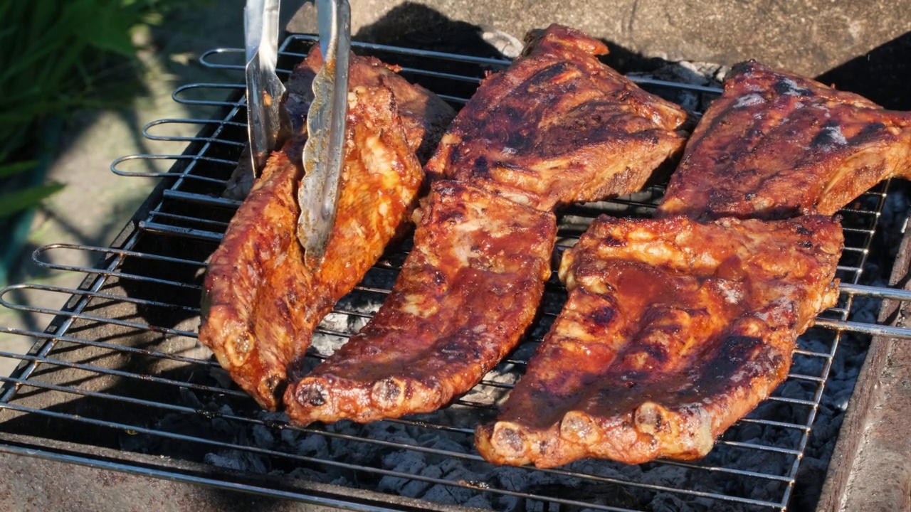 火焰烤架上的烤排骨。夏天的傍晚，人们在明火上烤排骨。美食户外午餐街头小吃慢动作特写视频素材