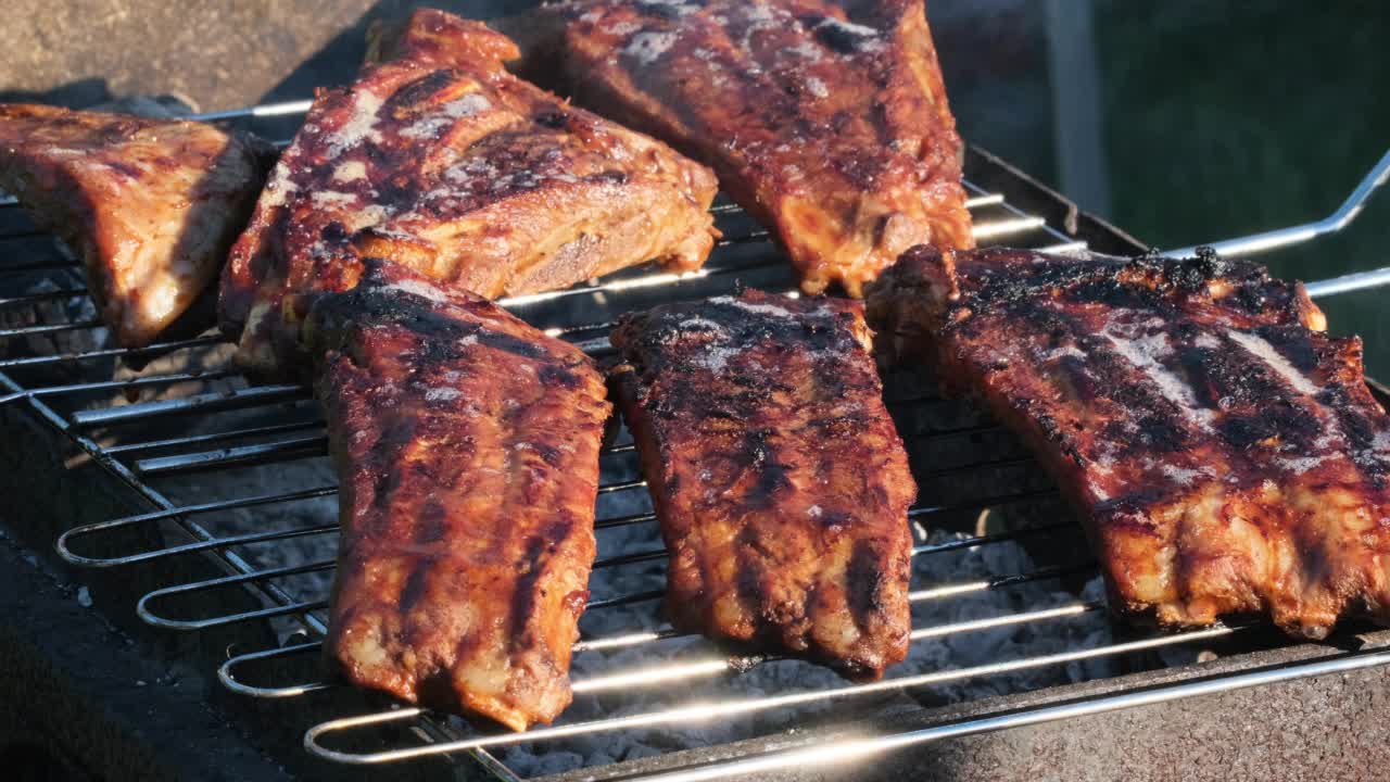 火焰烤架上的烤排骨。夏天的傍晚，人们在明火上烤排骨。美食户外午餐街头小吃慢动作特写视频素材