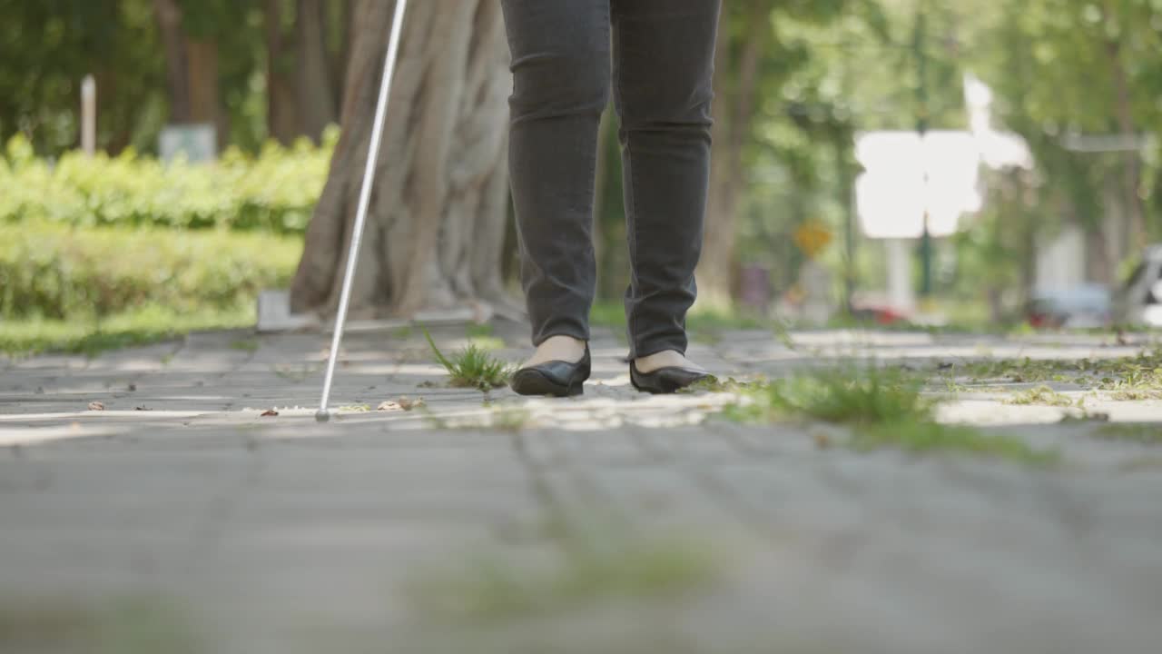 盲人残疾妇女在人行道上行走，包含触觉铺路引导块使用白色长手杖或盲人手杖一种移动工具，用于检测路径上的物体，视力受损的人。视频素材