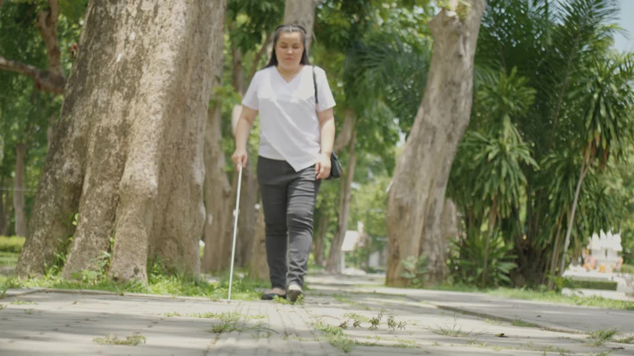 亚洲失明残疾妇女在人行道上行走包含触觉铺路引导块使用长白色手杖或盲人手杖一种移动工具，用于检测路径中的物体，视力受损的人。视频素材