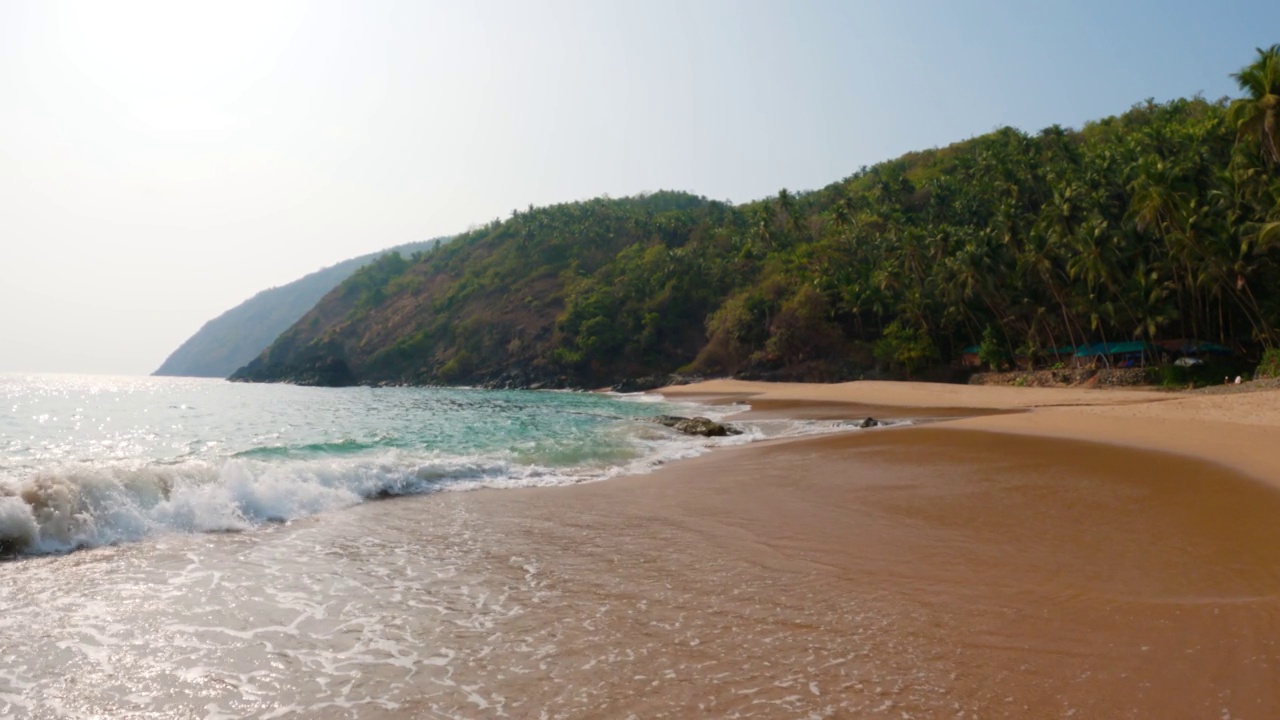 在印度南果阿的Kakolem海滩的热带海滩岸边的海浪的4K广角拍摄。热带沙滩岛上的海浪。在一个遥远的岛屿上，海浪拍打着海滩。视频素材