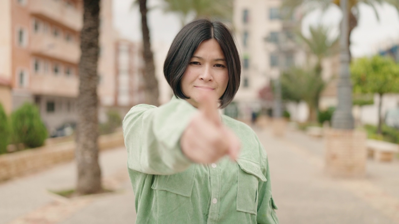 年轻的中国女子微笑着自信地在公园用手指做着手势视频素材