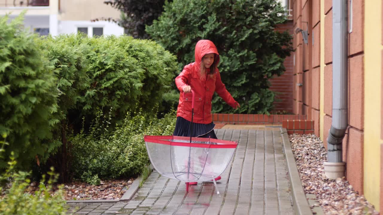 快乐的小女孩穿着红色雨衣和雨靴，撑着雨伞，喜欢在秋天的户外散步视频素材