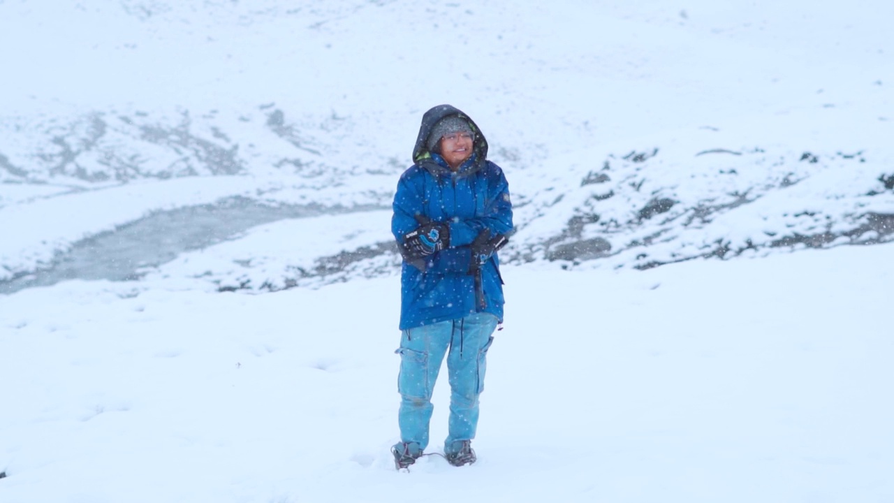 慢动作肖像年轻的印度女人站在喜马拉雅山脉在下雪期间，喜马偕尔邦，印度。在布里古湖徒步旅行期间，女性享受降雪。女性感觉冷视频素材