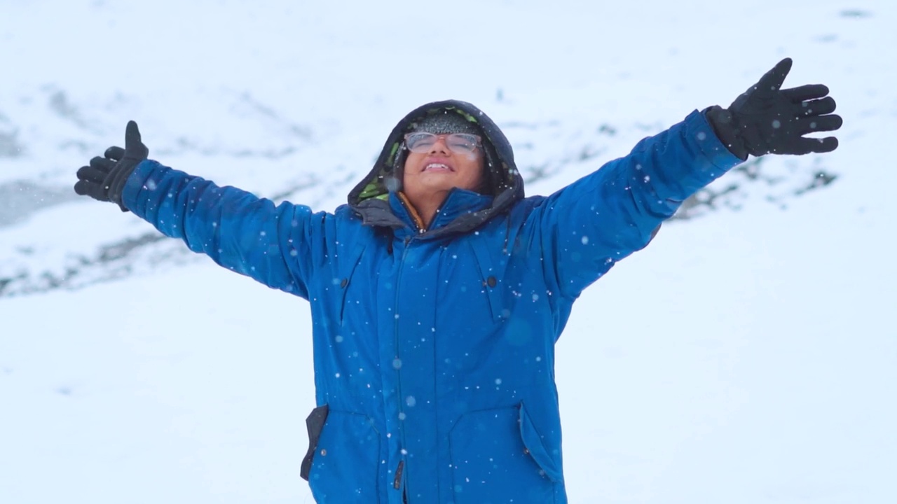 在印度喜马偕尔邦的马纳利，冬季的印度女旅行者在白雪覆盖的山上张开双臂享受降雪的照片。年轻女子享受降雪的慢动作镜头。视频素材