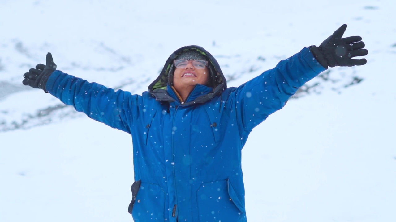 在印度喜马偕尔邦的马纳利，冬季的印度女旅行者在白雪覆盖的山上张开双臂享受降雪的照片。年轻女子享受降雪的慢动作镜头。视频素材