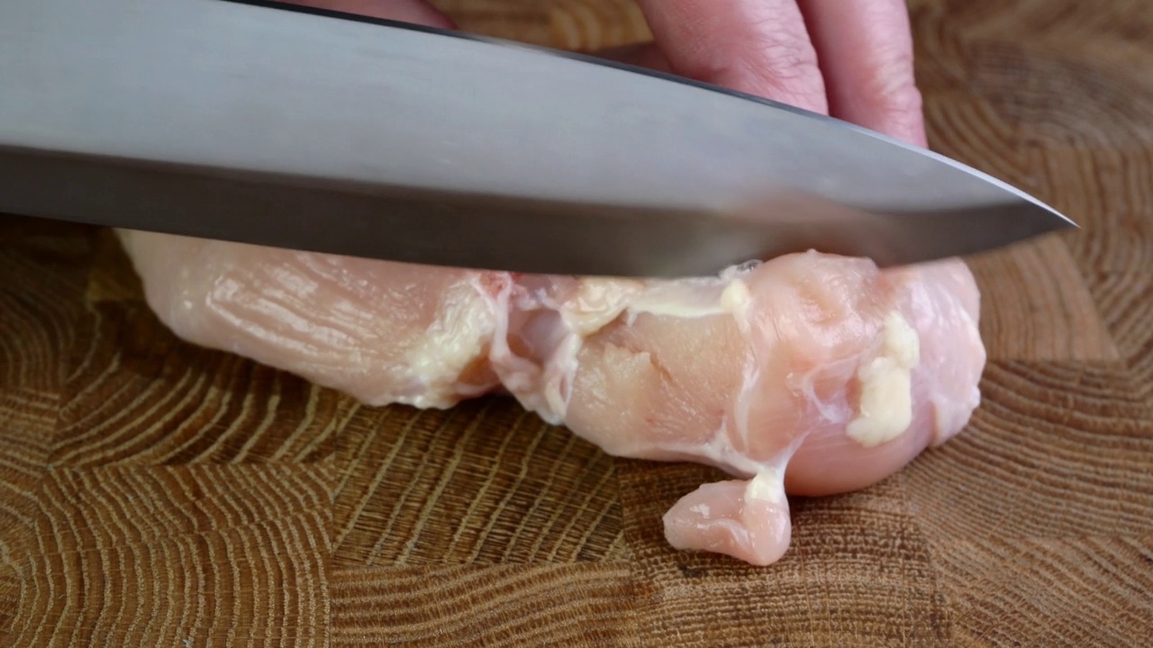 人手用刀把生鸡肉或火鸡胸肉切成片放在砧板上。视频素材