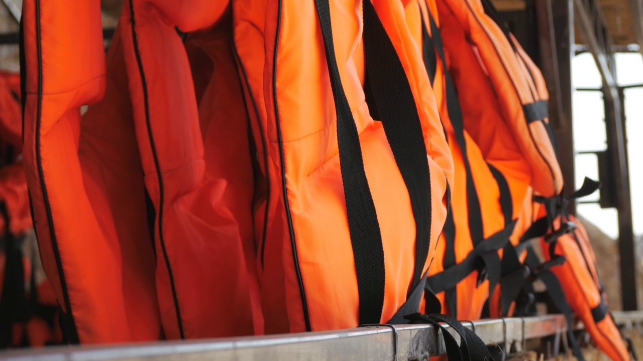 橙色救生衣在海边储备。许多救生衣排成一排挂在衣架上。船舶租赁商店的安全防护服。视频下载