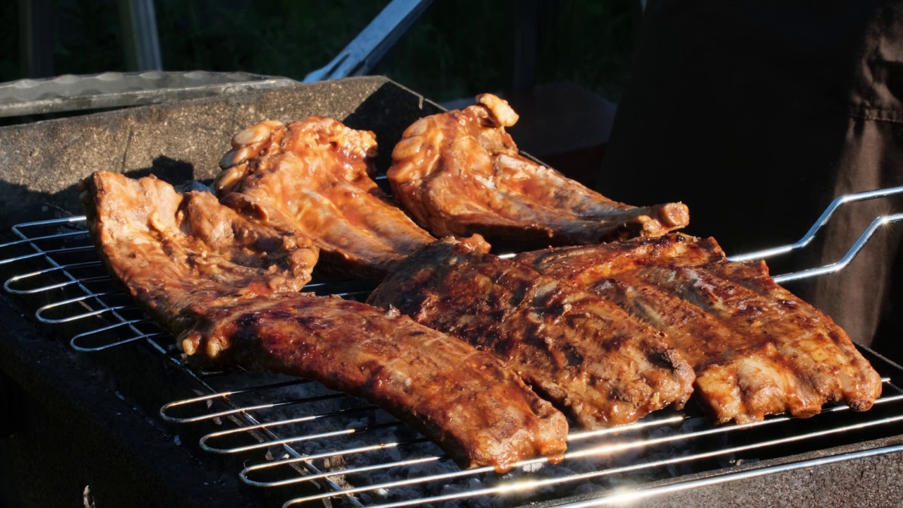 火焰烤架上的烤排骨。夏天的傍晚，人们在明火上烤排骨。美食户外午餐街头小吃慢动作特写视频素材