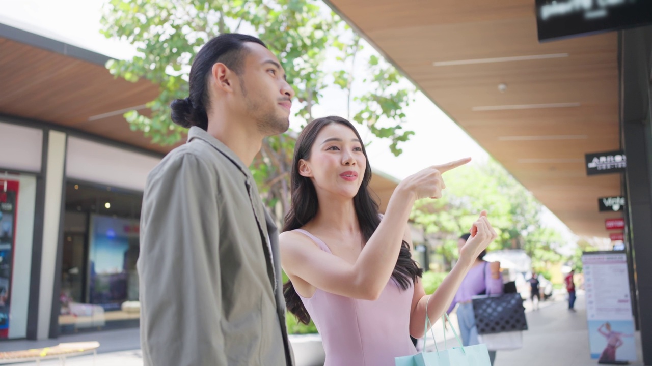 亚洲青年男女在百货公司户外购物。迷人的情侣拿着购物袋，然后幸福地走在一起，享受购物中心购物。视频素材