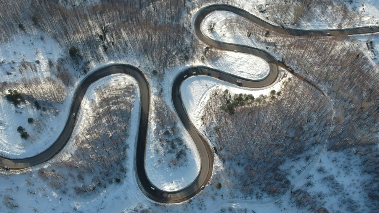 弯曲的山路。天气寒冷，还下着雪。山道上汽车的鸟瞰图。视频素材