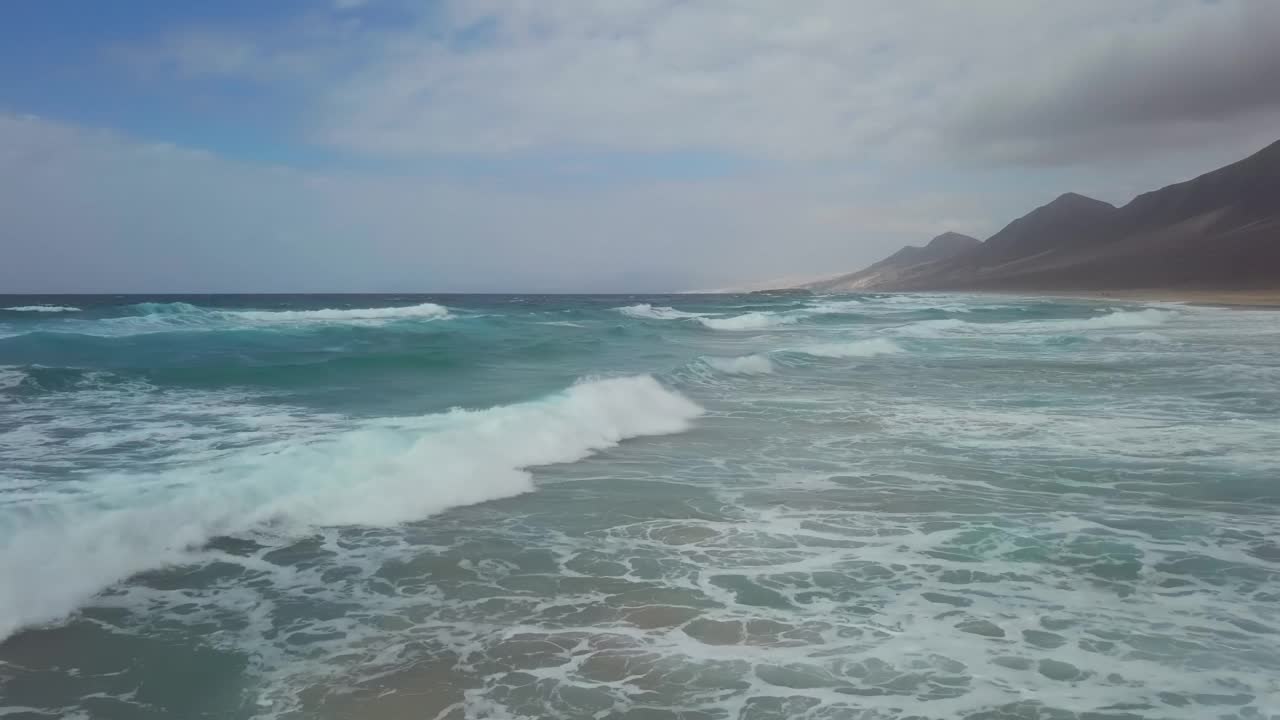 西班牙加那利群岛富埃特文图拉的简迪亚半岛，低空飞行的海浪拍打着沙漠沙滩普拉亚德科菲特海滩视频素材