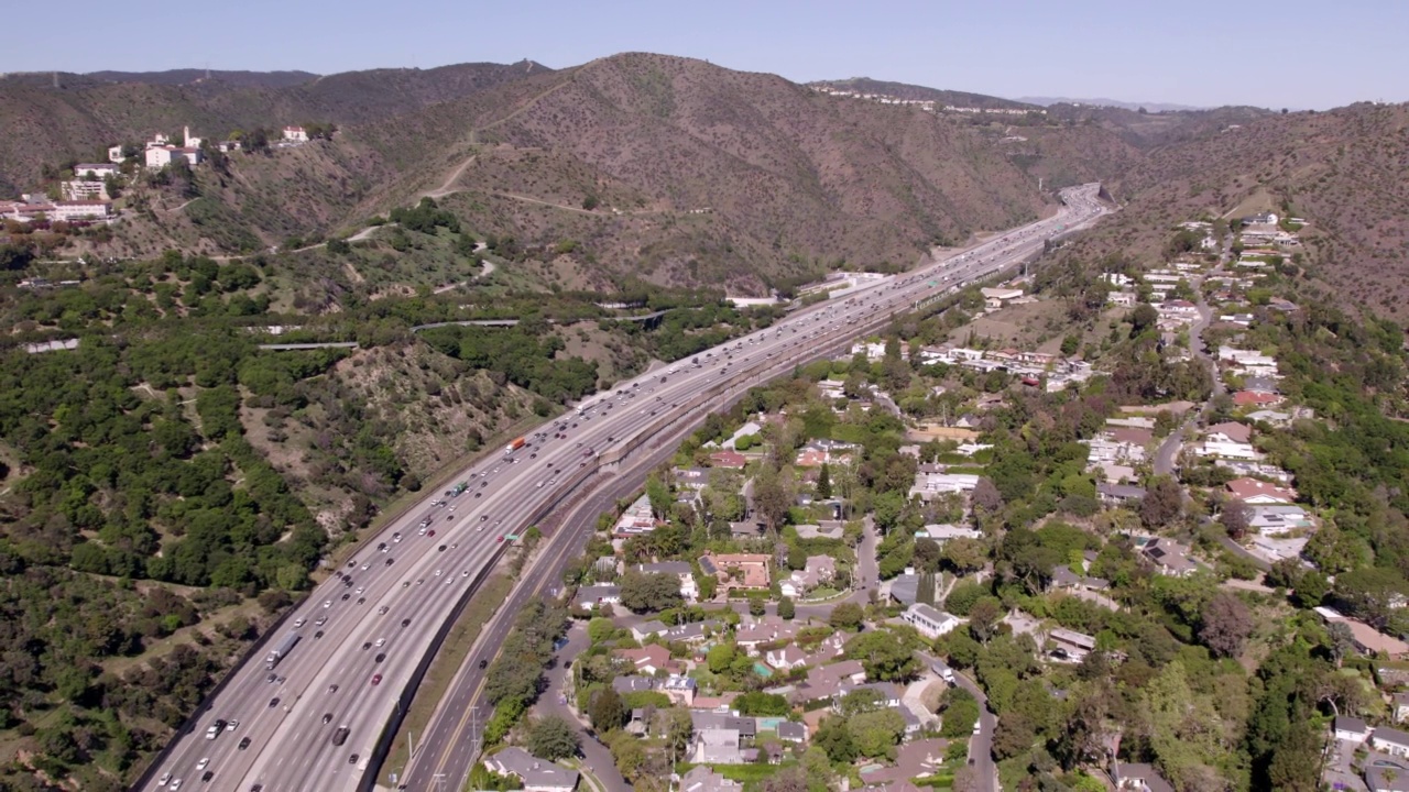 航拍时移拍摄汽车在道路上移动的自然山，无人机在城市的房子上向后飞行-比弗利山，加州视频素材