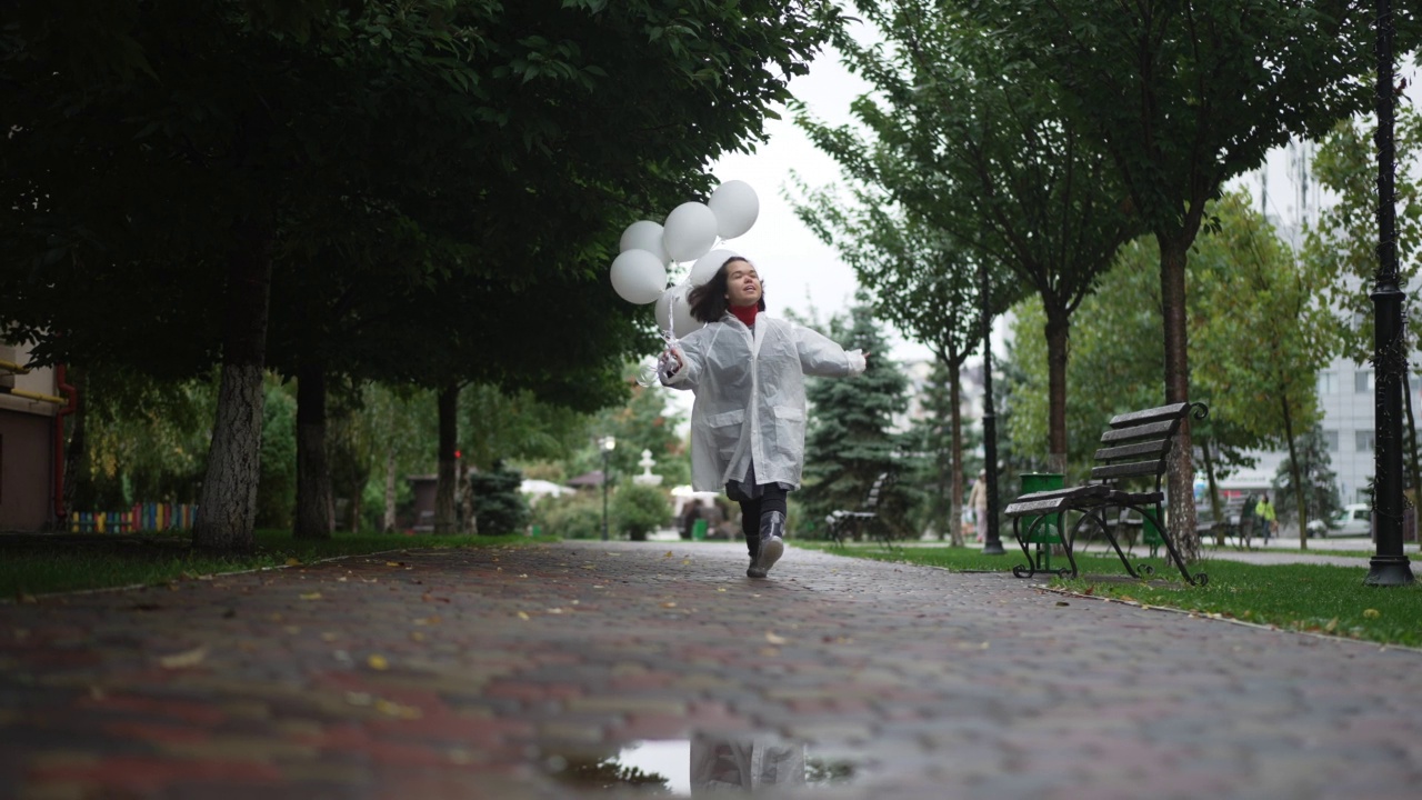 广角镜头兴奋的快乐的小人物跳跃的气球微笑享受悠闲的雨天。幸福的白人小女人的肖像休息在城市户外有乐趣。视频素材