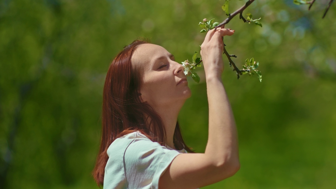 美丽的女人在春天盛开的花园里闻着苹果树的花，4K, Prores视频素材