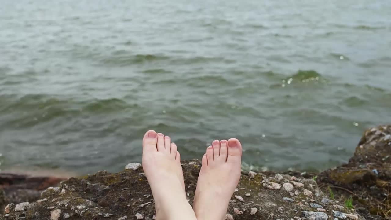 腿和海洋。概念视频。女人的双腿以湖水的波浪为背景。这个女孩躺在海洋、湖泊、河流、水库上享受暑假。视频素材