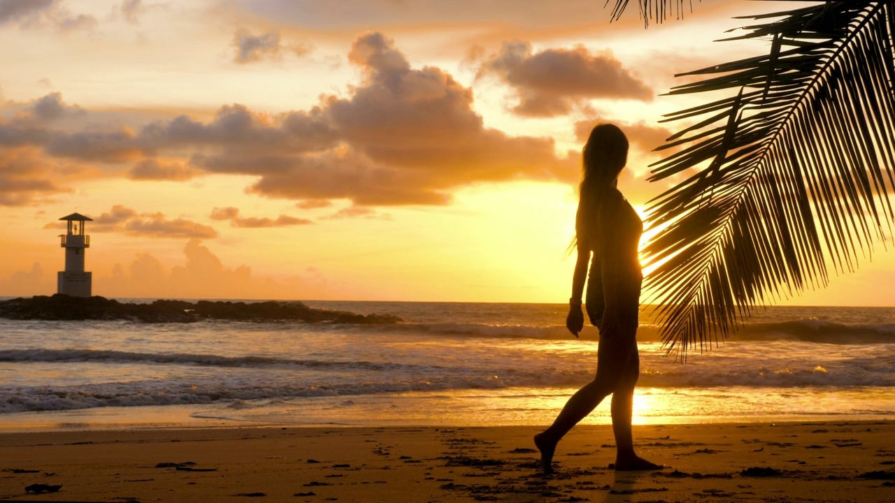 女游客赤脚走在沙滩上的海浪。年轻女子走在海边浪漫的金色夕阳灯光。快乐女孩享受暑假假期在海洋。慢动作视频素材