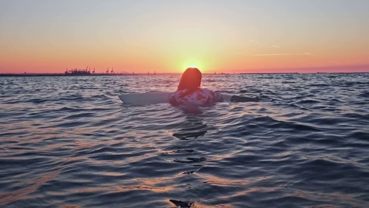 穿着长袖泳衣的女性冲浪运动员在平静的海浪中漂浮在冲浪板上视频素材