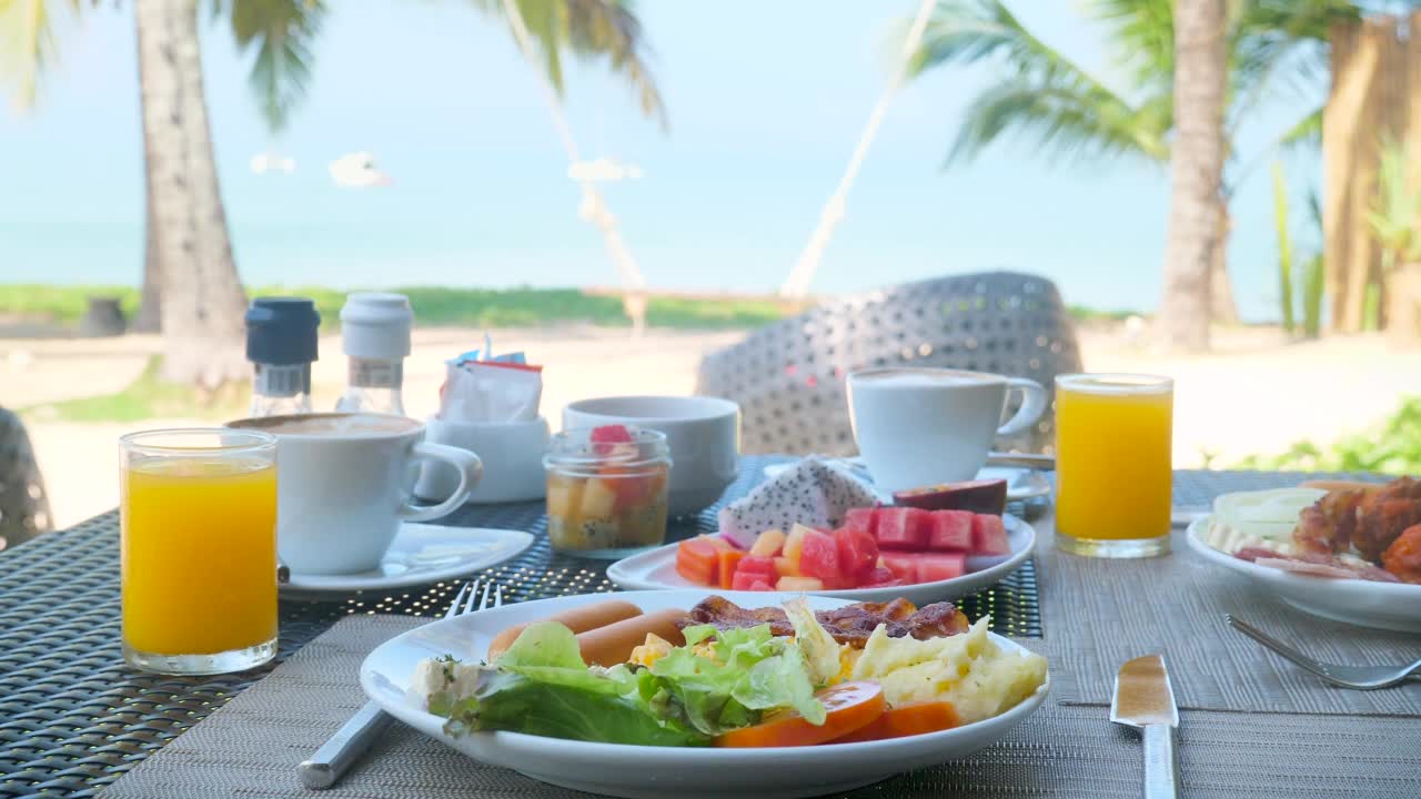 豪华的双人早餐餐桌，健康的食物，美丽的热带海景和棕榈树的背景。酒店上午，暑假。旅游理念，海洋度假。视频素材