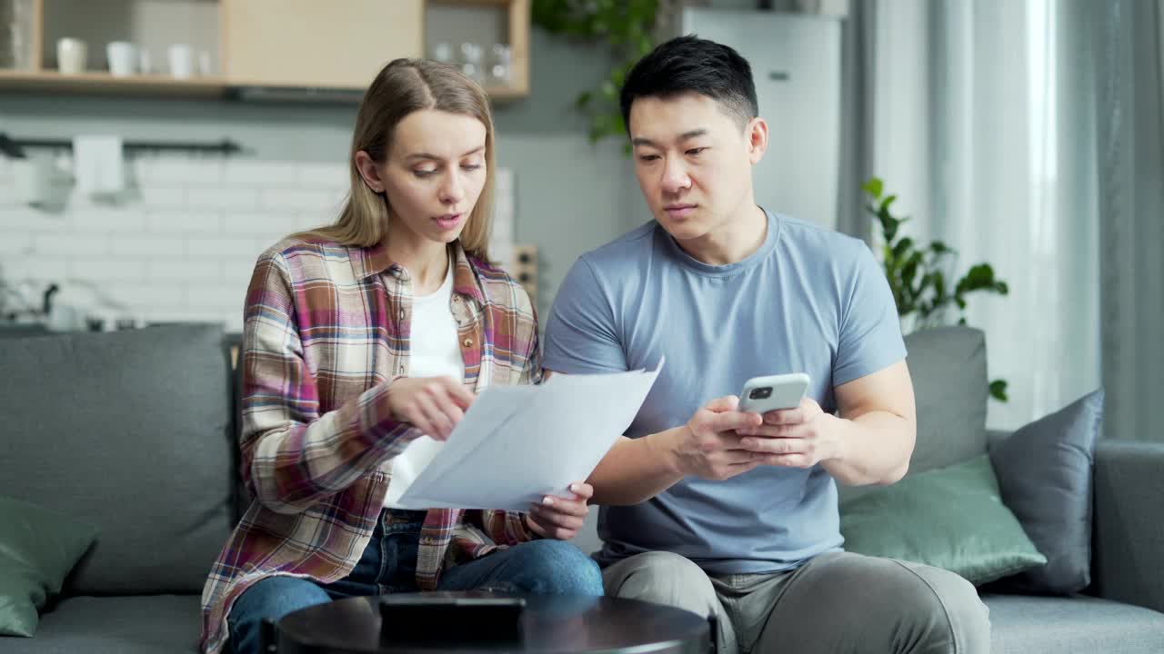 年轻的家庭夫妇使用网上银行应用程序通过电话。男性和女性支付服务，输入数据文件，使用应用程序，在家里的智能手机视频素材