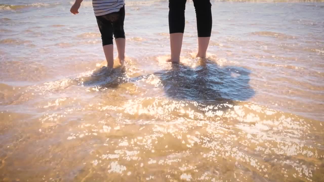 母女俩在海滩上把脚浸在海水里视频素材