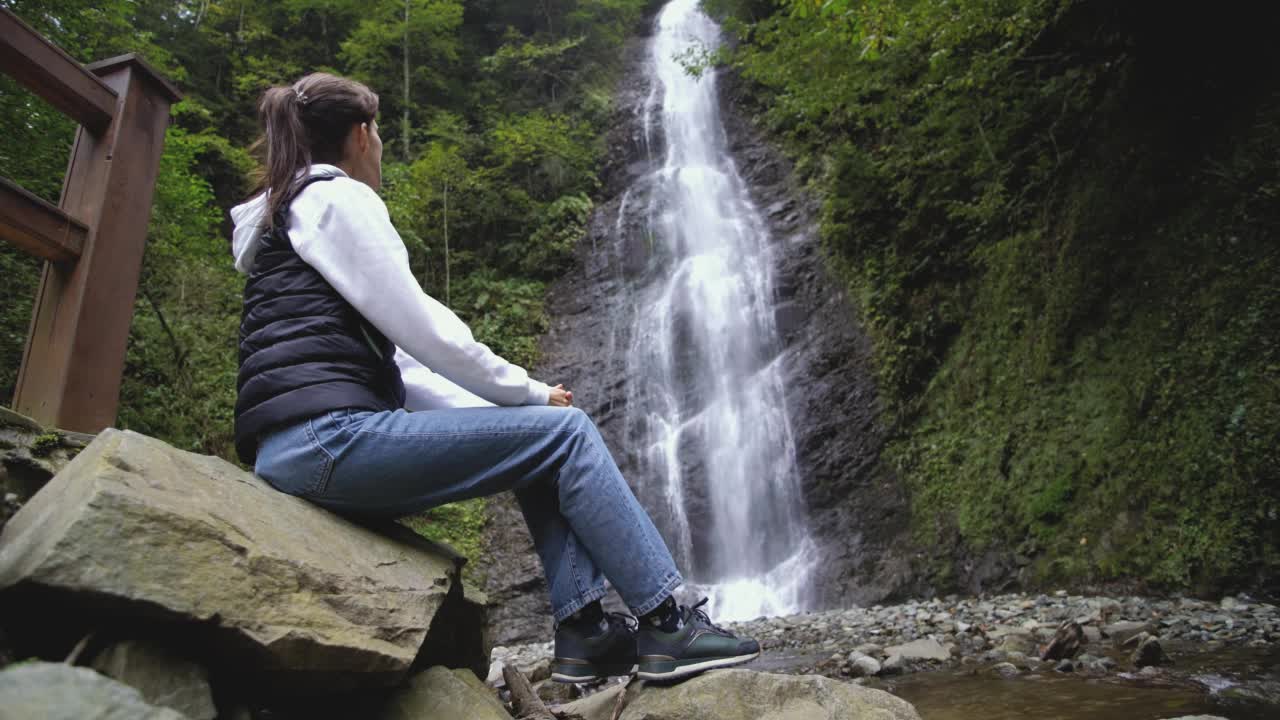 一位年轻女性旅行者欣赏瀑布的背影视频素材