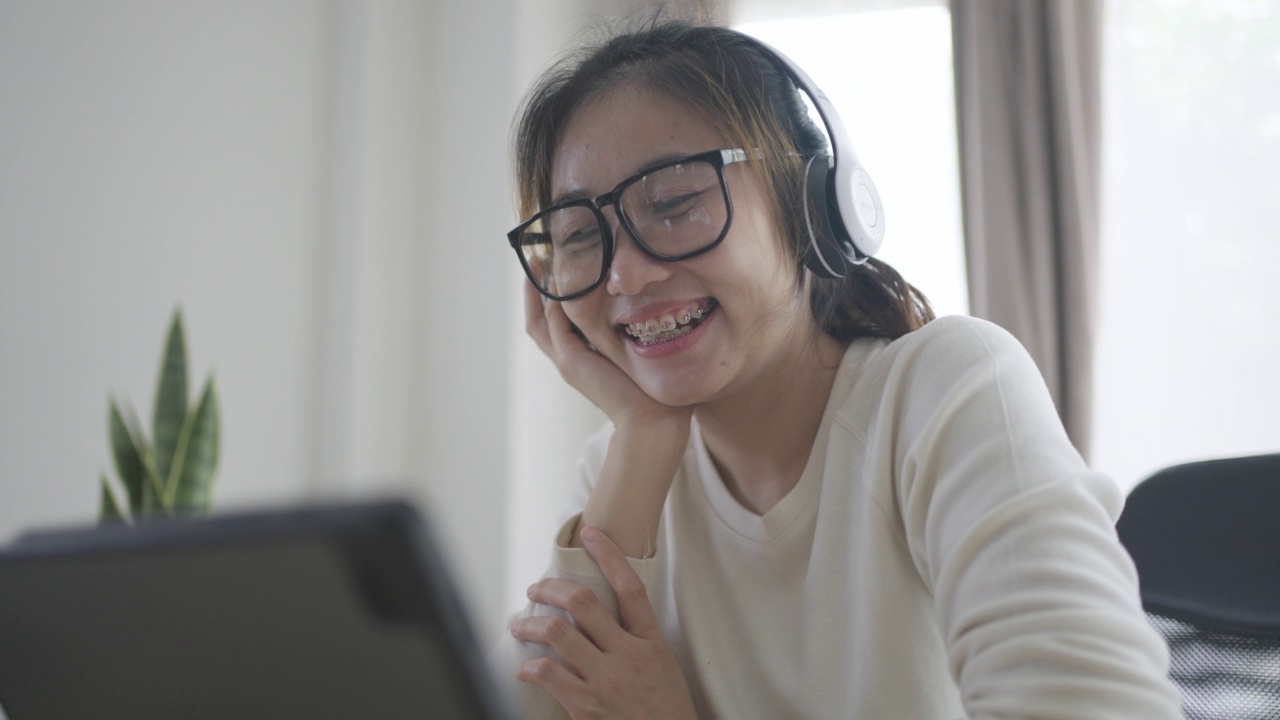 年轻的亚洲女性放松在沙发上，听音乐与耳机在家里的客厅视频素材