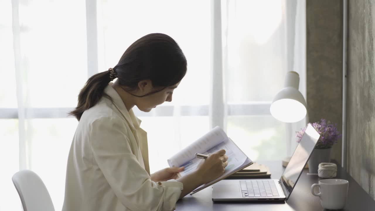 亚洲女性会计，处理财务图表文件，为图表和家庭收入图表报告计算税收。在笔记本电脑上工作并计划费用预算的女商人。视频素材