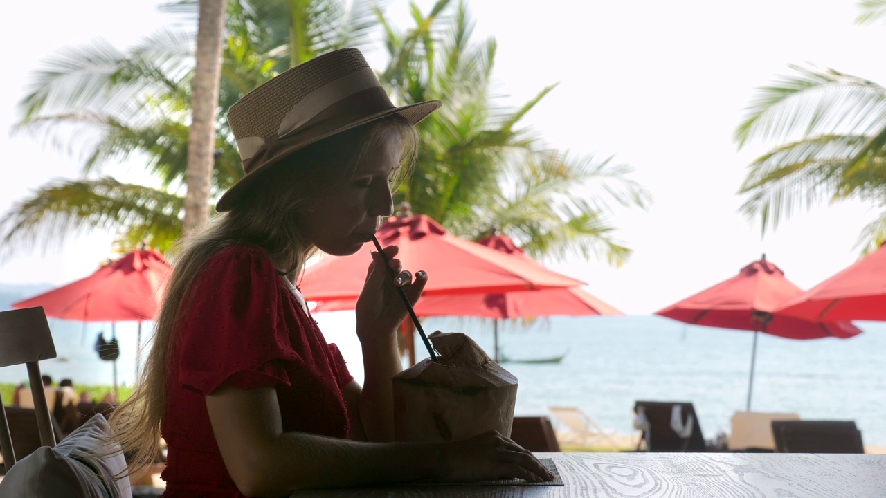 热带度假。旅游女孩喝年轻的椰子汁在户外海滩咖啡馆。热带海滩度假胜地的女性游客视频素材