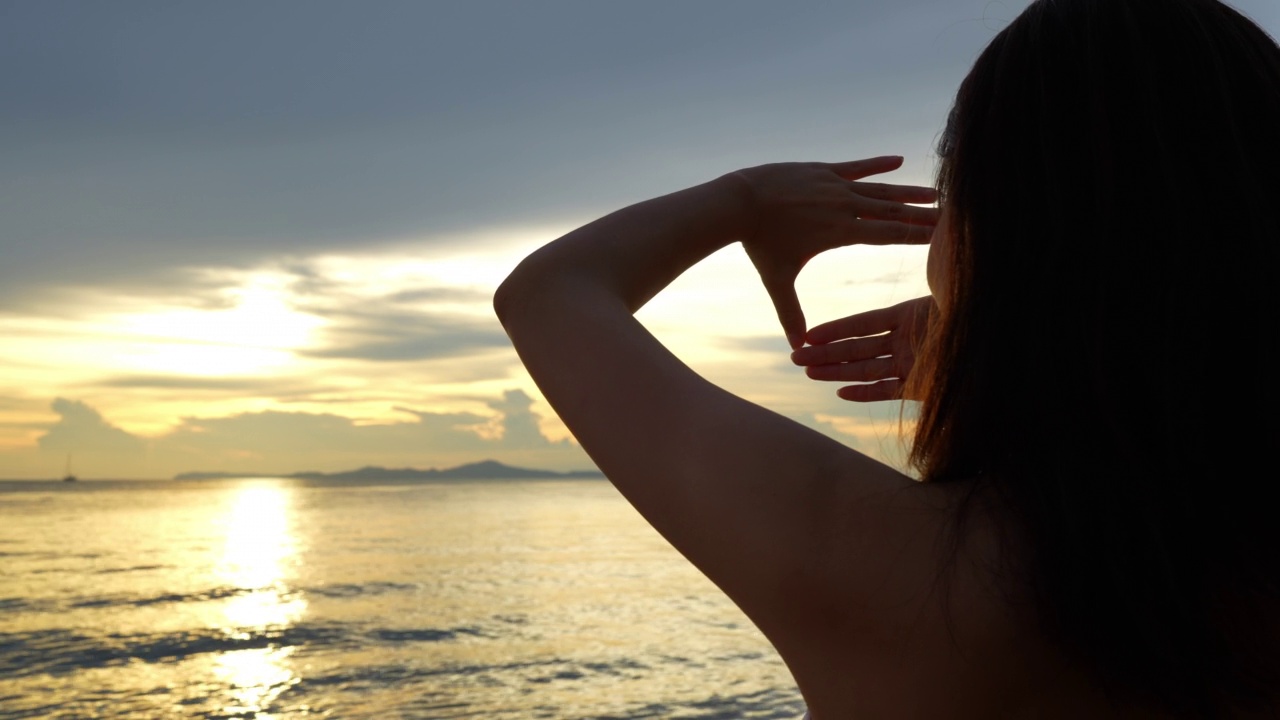 女性在夕阳西下的沙滩上挥挥手，享受热带的休息和放松的旅行生活方式，快乐的女性比基尼泳装自由地度过暑假时光。视频素材