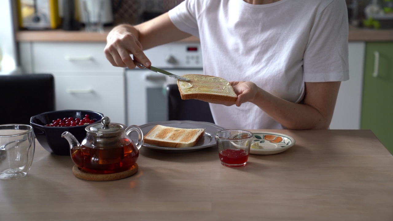 女人在做早餐的果酱三明治，女人的手在烤面包片上抹黄油视频素材