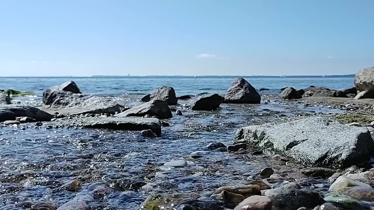 阳光明媚的日子，从小溪或河流流入大海的低角度观水视频素材