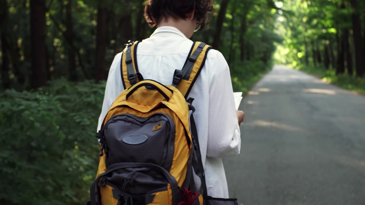 一个背着明亮双肩包的女游客移动着，手里拿着一张旅游地图，旅游路线视频素材