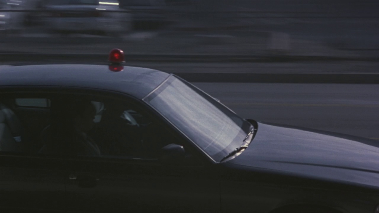 中等跟踪镜头黑色警车在城市街道上超速驶过其他车辆。波夫从街边的大楼里往窗外看。底片剪视频素材