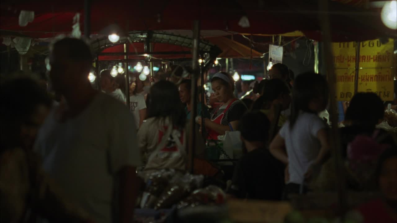 泰国街头市场帐篷下购物的男女。可能是农贸市场。汽车在前景缓慢驶过视频素材