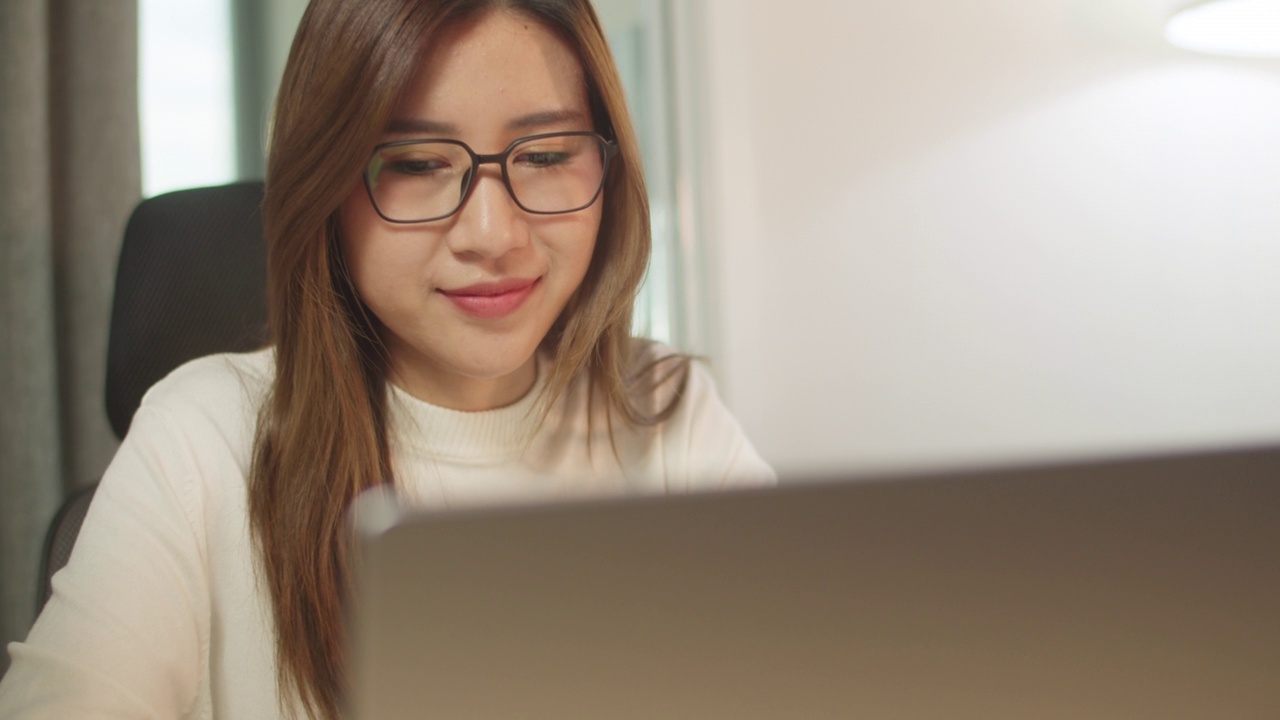 一位戴眼镜的年轻女子坐在电脑前在家办公。视频素材