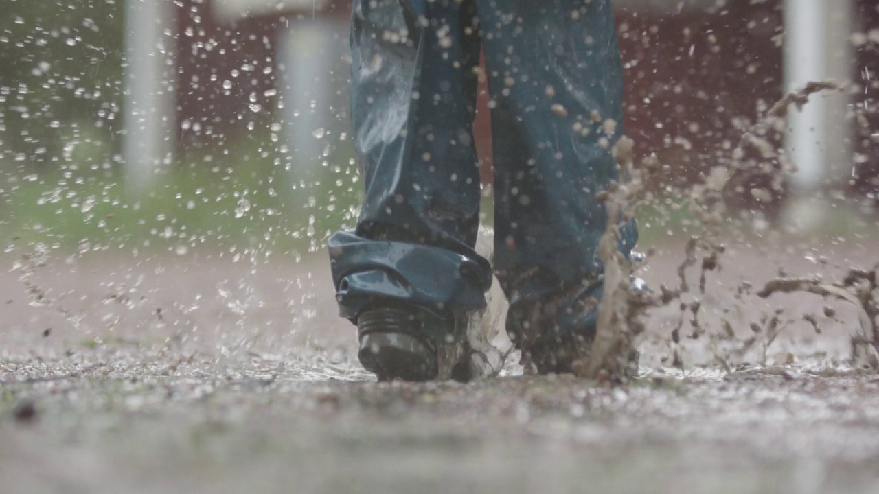 慢动作——大雨中，一个孩子在泥泞的水坑中跳跃视频素材