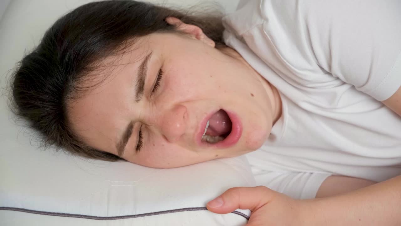 一位30岁的黑发女子躺在床上的枕头上打哈欠。视频素材