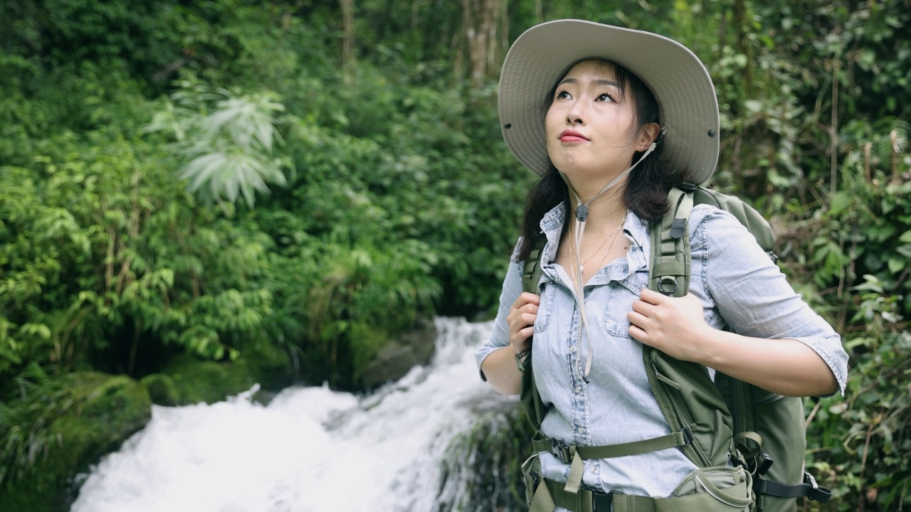 一位年轻女子站在山上的一条小溪边徒步旅行视频素材