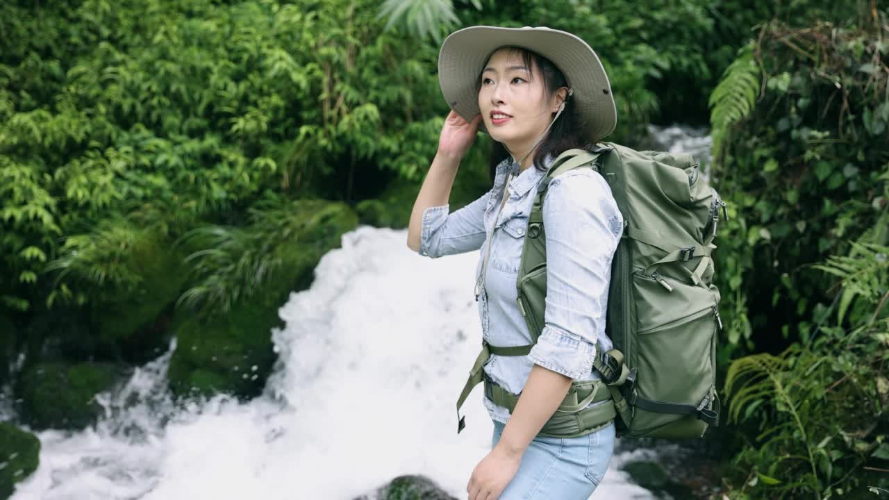 一位年轻女子站在山上的一条小溪边徒步旅行视频素材