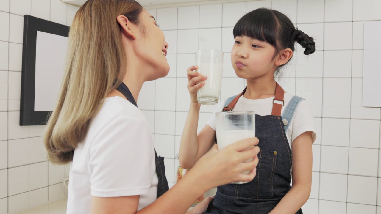 亚洲家庭在客厅享用早餐。小女孩女儿坐在桌子上，和微笑的爸爸妈妈在早上喝牛奶。家庭幸福。视频素材