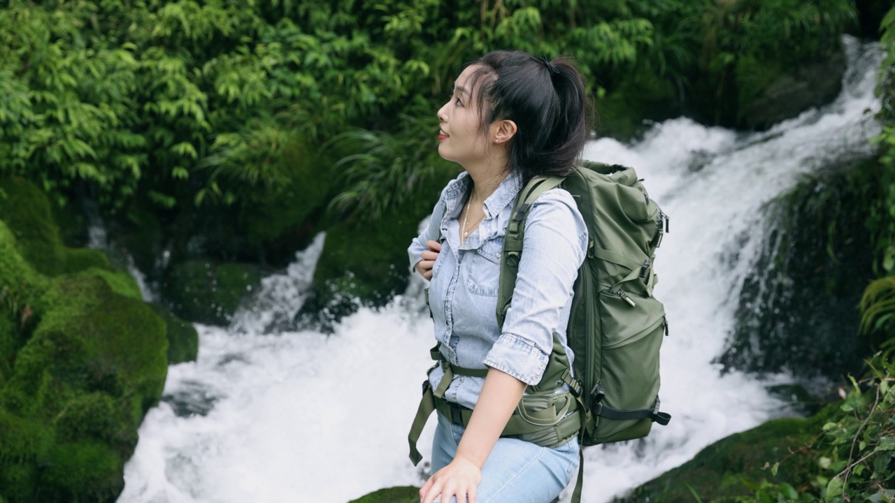 一位年轻女子站在山上的一条小溪边徒步旅行视频素材