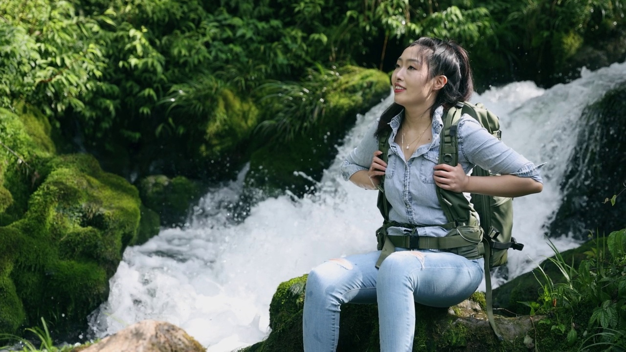 坐在大自然瀑布旁的女徒步旅行者视频素材